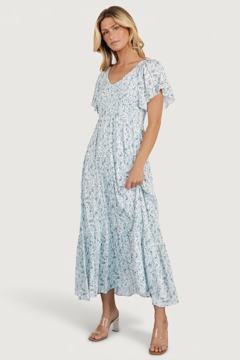 Model wearing Joanie smocked dress in white and sage, full-length view showing empire waist, flowy single-tier skirt, and hidden pockets.