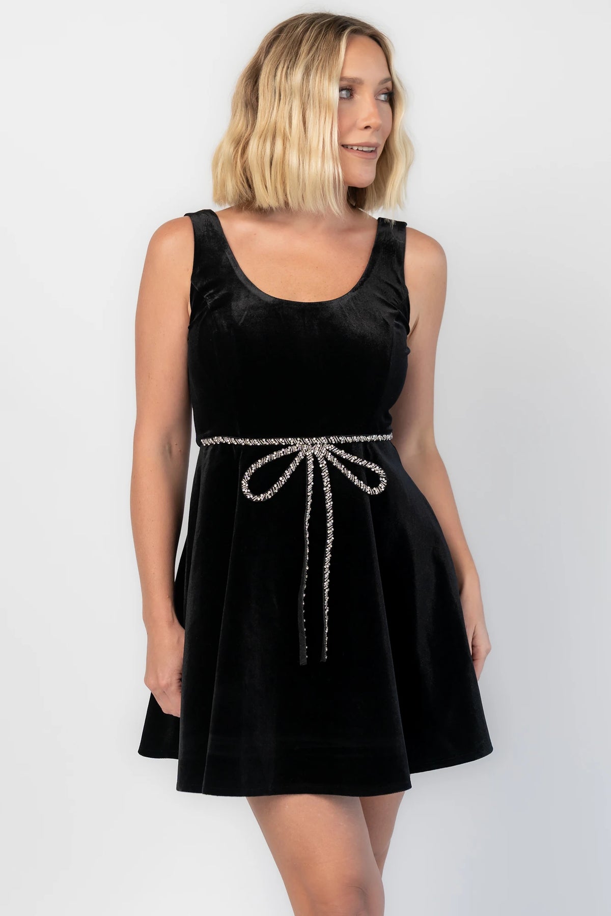 Julieta Short Dress in Black with a velvet finish, scoop neckline, and a rhinestone bow at the front waist.