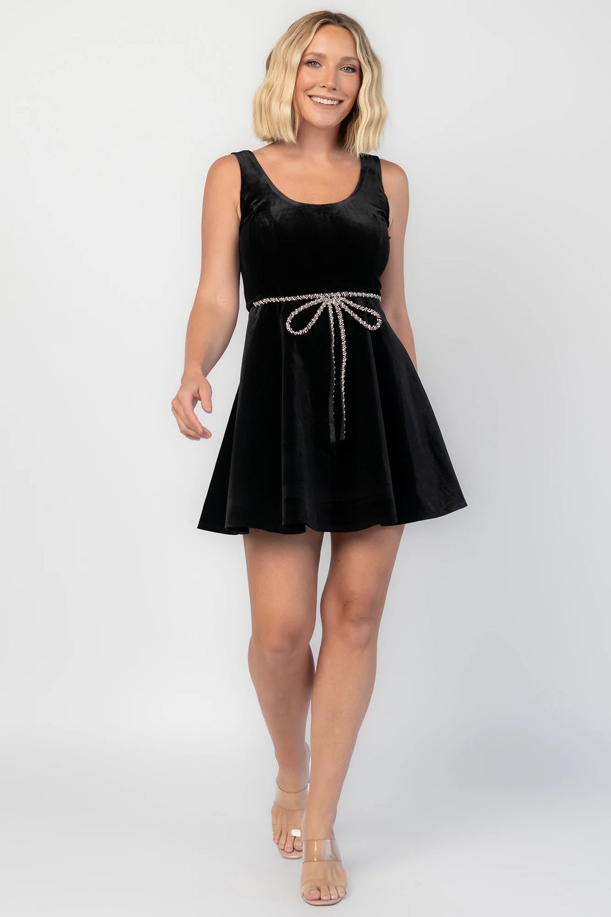 Julieta Short Dress in Black with a velvet finish, scoop neckline, and a rhinestone bow at the front waist.