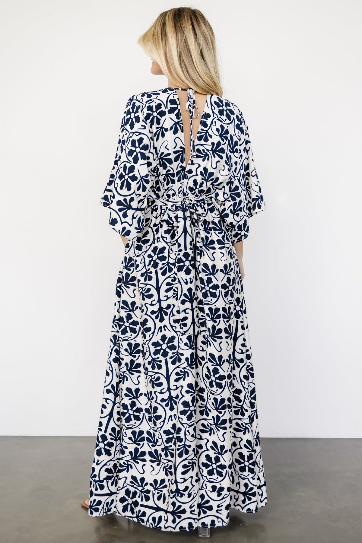 Back view of the Juna dress showing the V-back with tie, elastic paneled waist, and the graceful fall of the maxi hem.