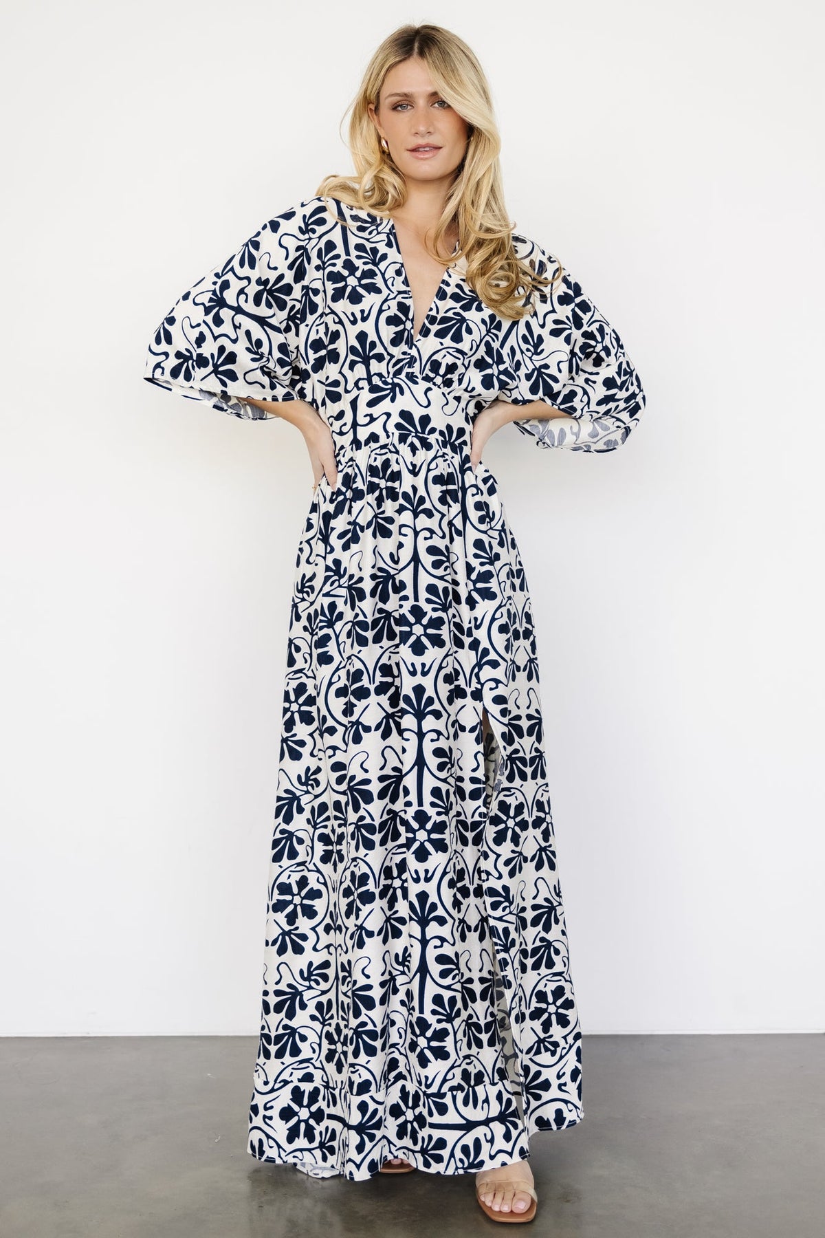 Three-quarter view of the dress on a model highlighting the elastic back waist, attached tie, and soft ivory fabric with navy print.