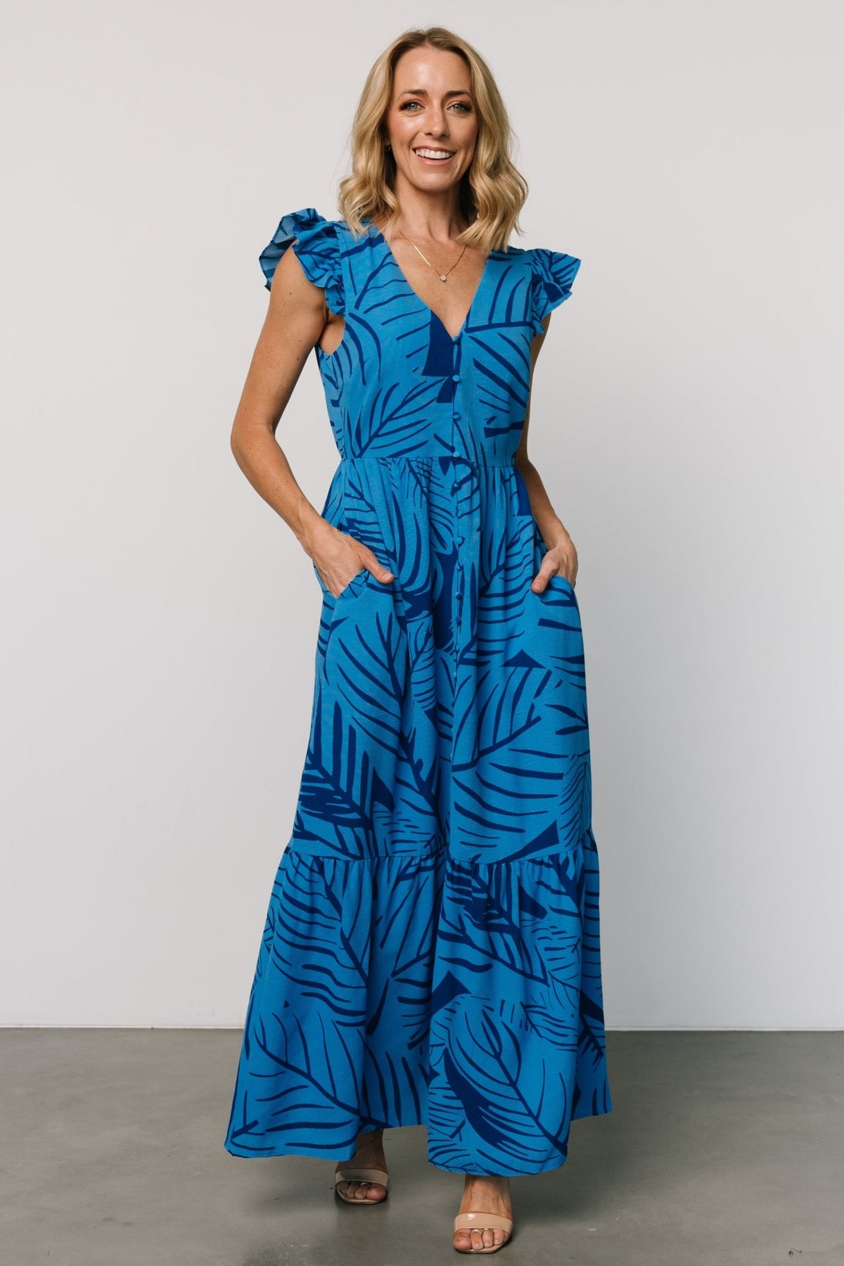 Model front pose wearing Kaia Button Maxi Dress in blue print, showing full length, soft drape, and V-neck styling for warm-weather occasions.