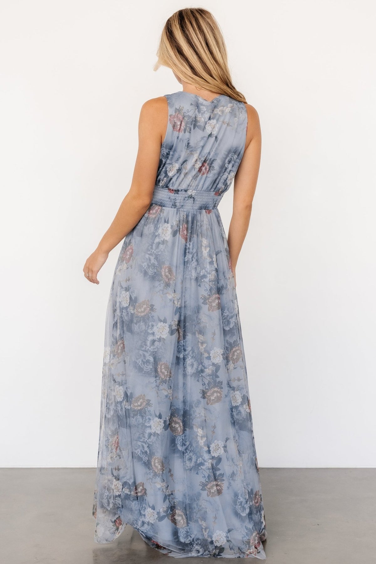 Back view of dusty blue floral tulle maxi dress on model, showing full lining, flowing skirt, and tank-style sleeve detail.