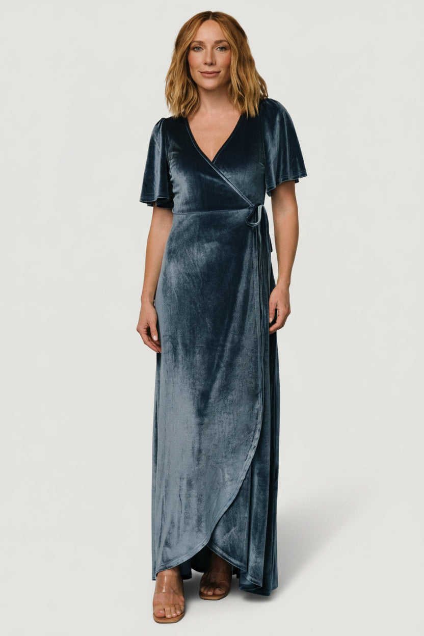 Three-quarter angle of velvet wrap dress in soft blue highlighting tulip-style skirt, drape and fabric texture in motion.
