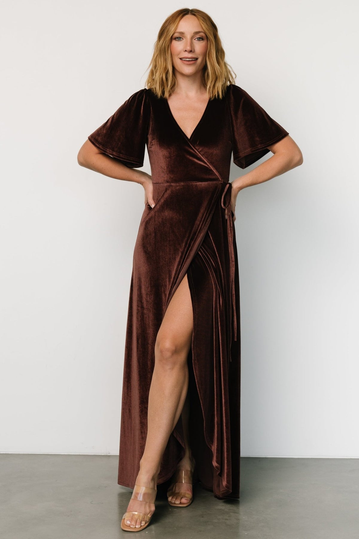 Three-quarter angle of the clove velvet wrap dress highlighting the drape, waist tie loop, and gentle stretch of the fabric on a standing model.