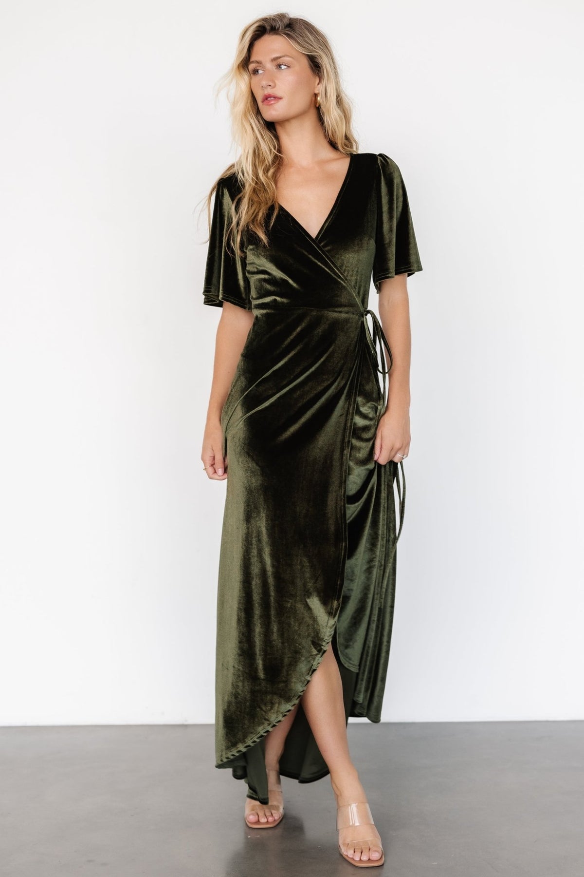 Studio shot of the Katelyn Velvet Maxi Wrap Dress in dark olive on a neutral background, showing front styling and sleeve detail.