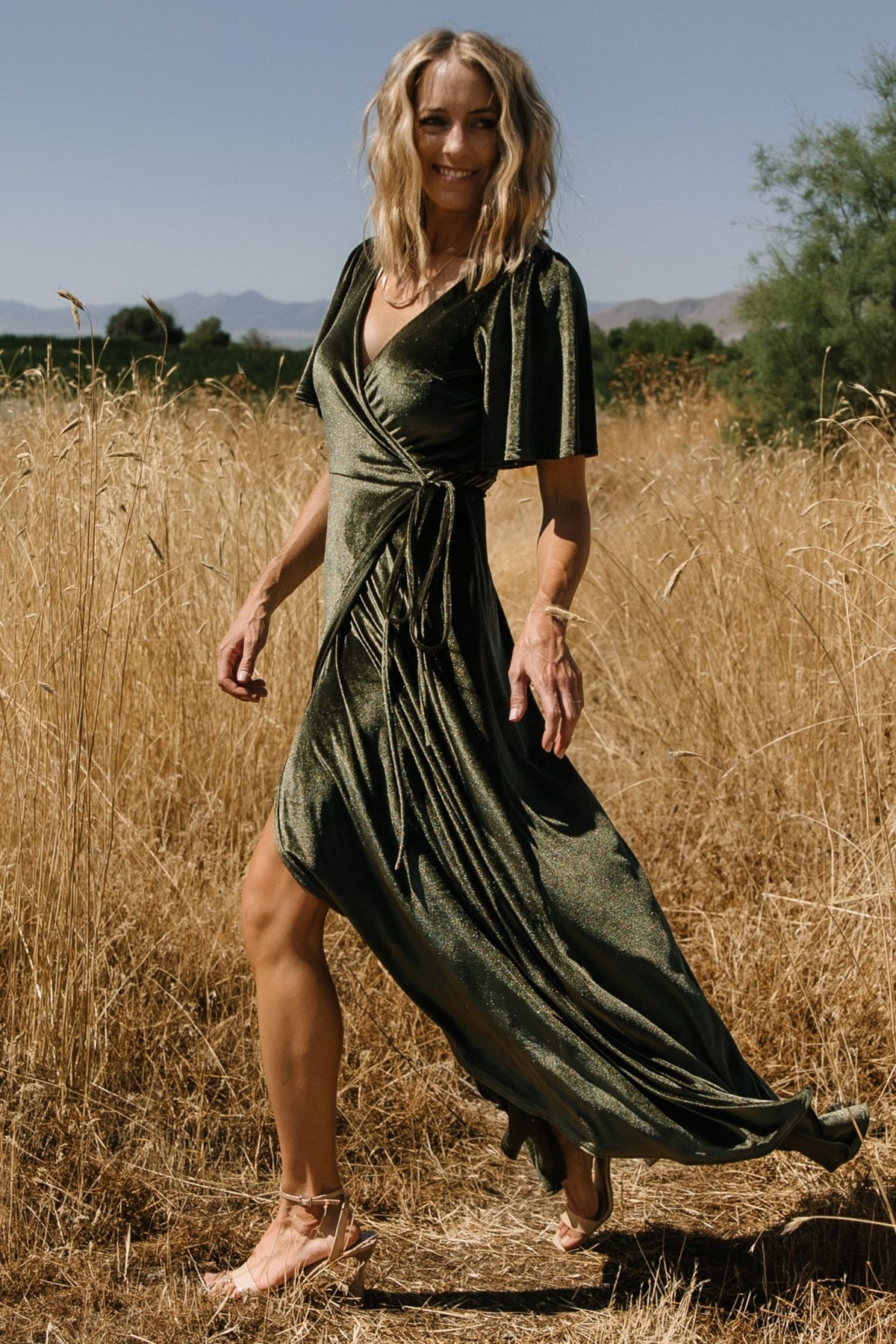 Back and movement shot of the velvet wrap maxi in dark olive, showing full lining, skirt flow, and sleeve length on model.