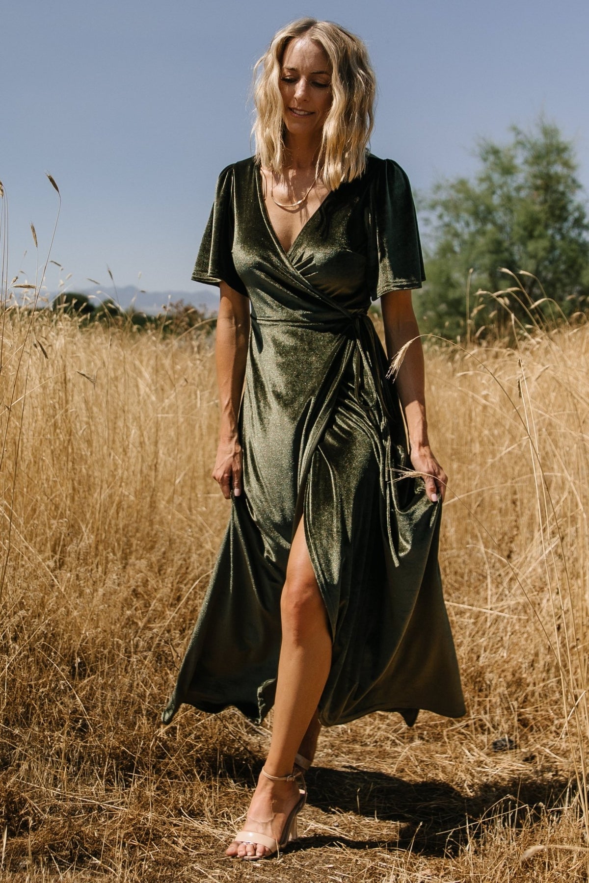 Front view of the Katelyn Velvet Maxi Wrap Dress in dark olive on a model, showing the V-neck, flutter sleeves, and tulip skirt in soft velvet.