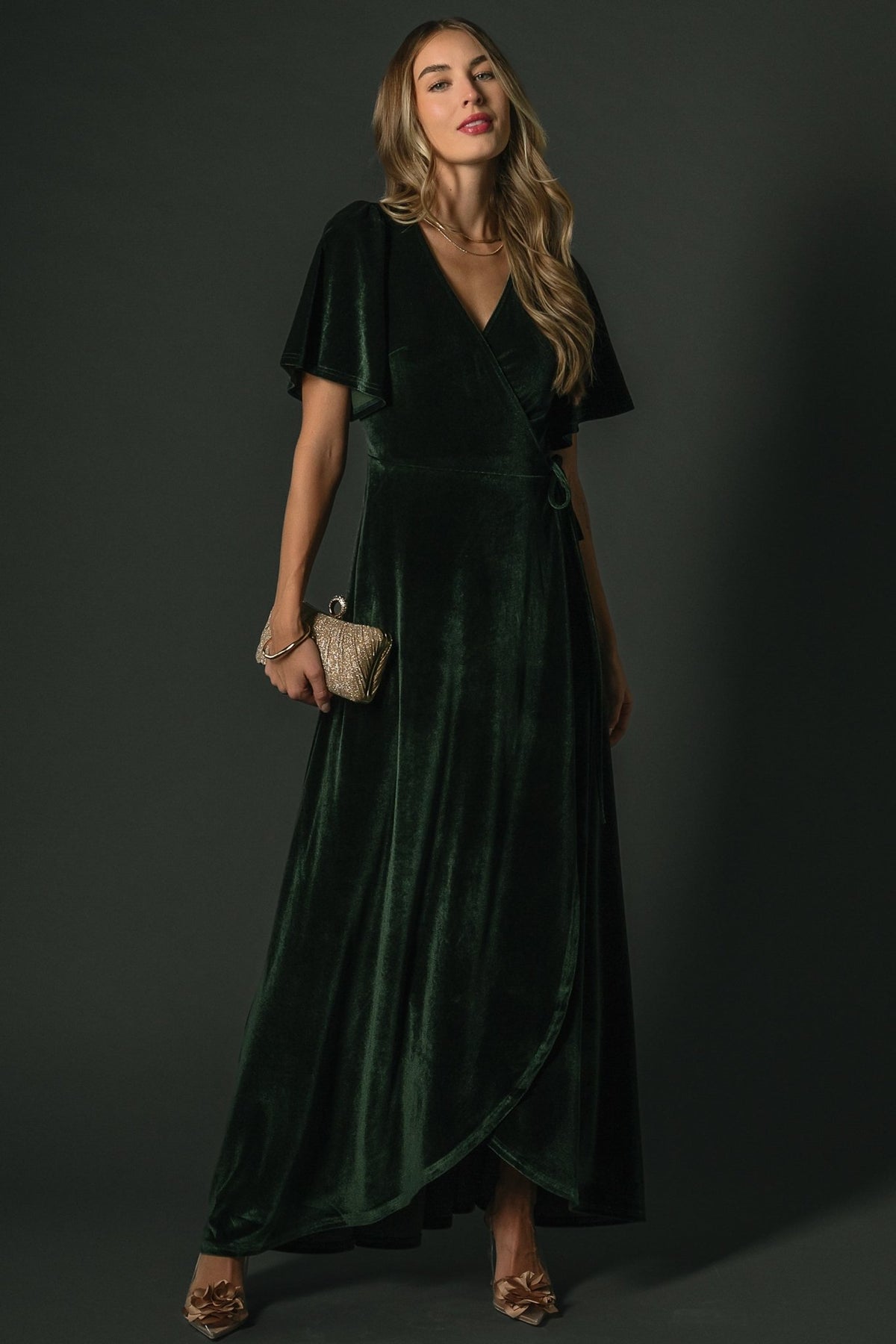 Front view of deep green velvet maxi wrap dress on model, showing higher-coverage V-neck, flutter sleeves, and tulip skirt (lined).