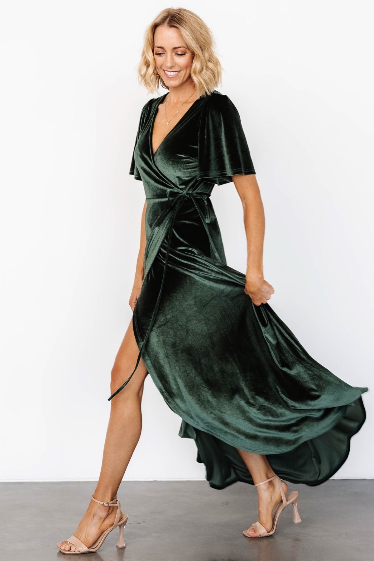 Styled shot of deep green velvet dress on model for formal occasion, showcasing luxe texture and tulip skirt movement.