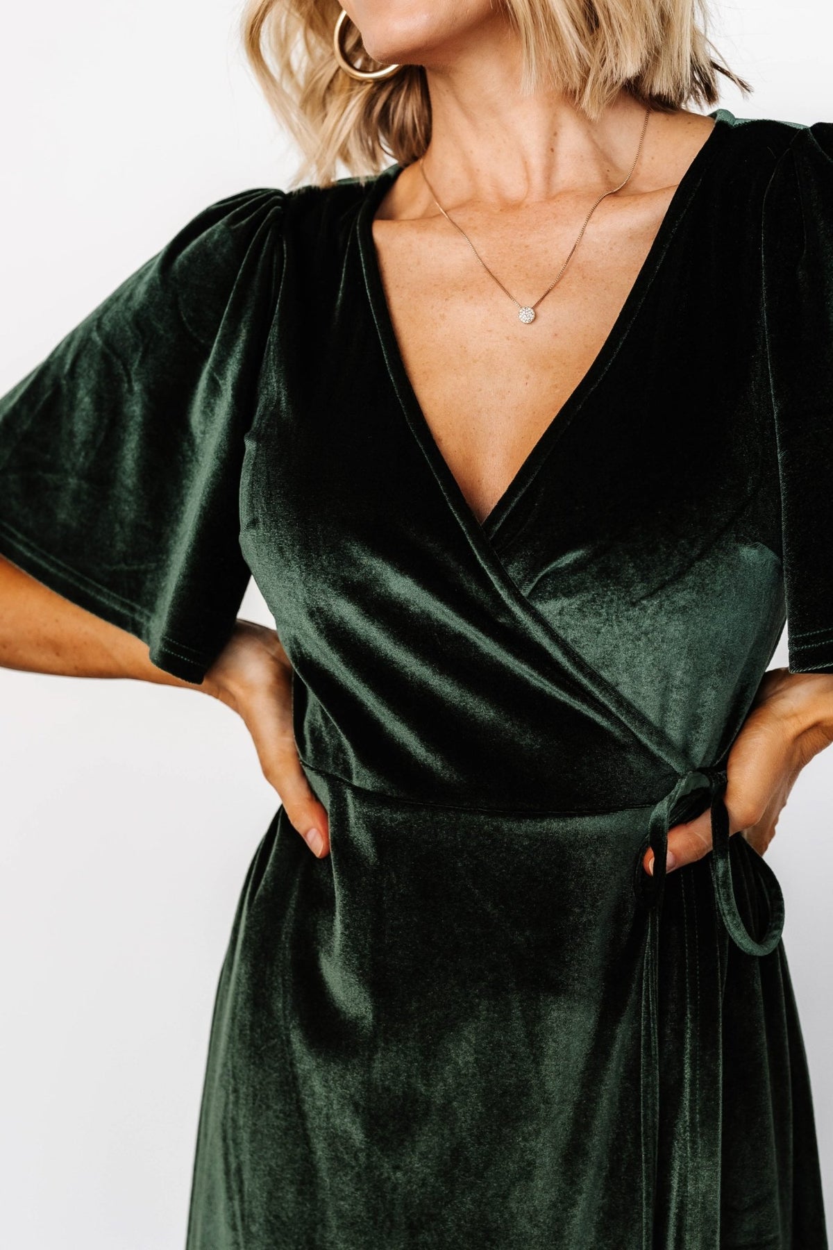 Model wearing the deep green wrap dress walking to show movement of the tulip-style skirt and flutter sleeves.