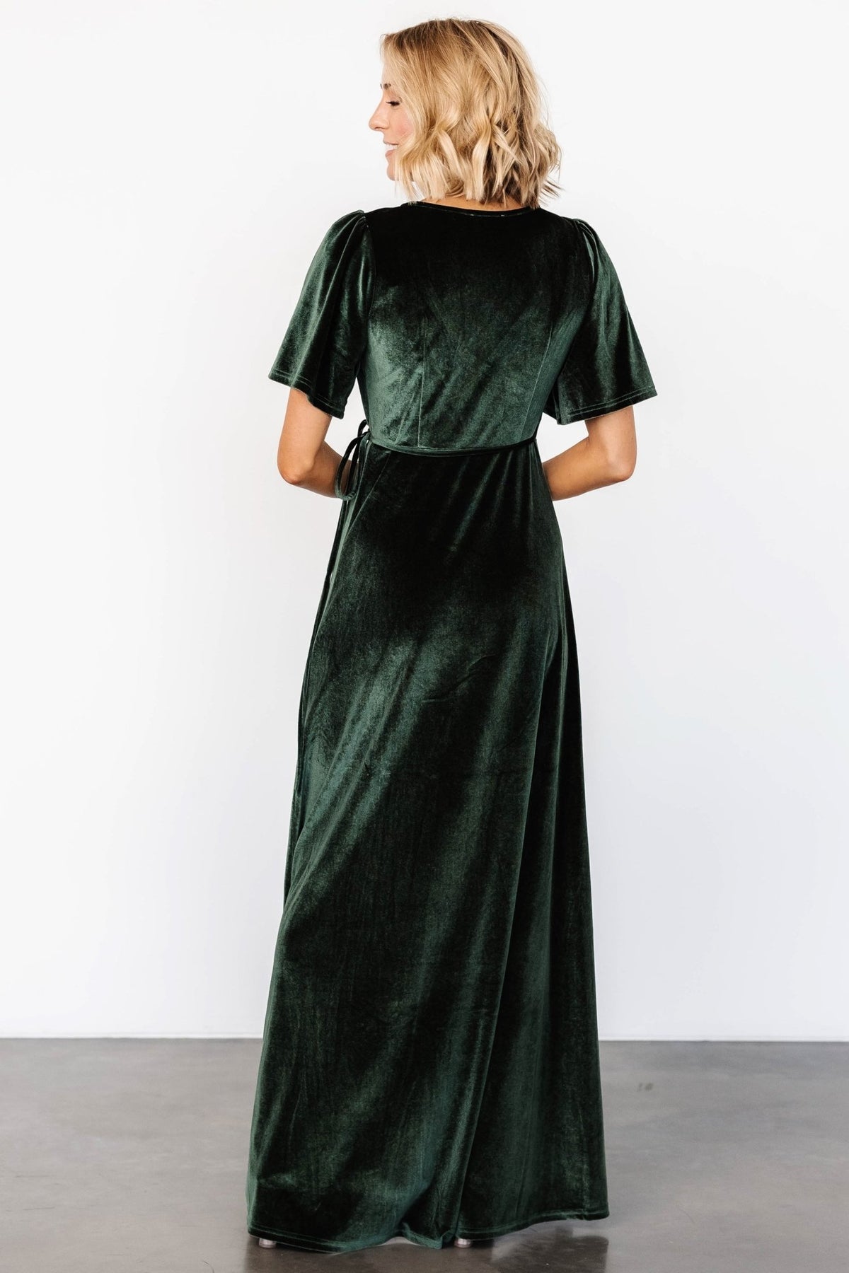 Model posing in deep green velvet wrap dress to illustrate sleeve length, V-neck coverage, and overall silhouette.