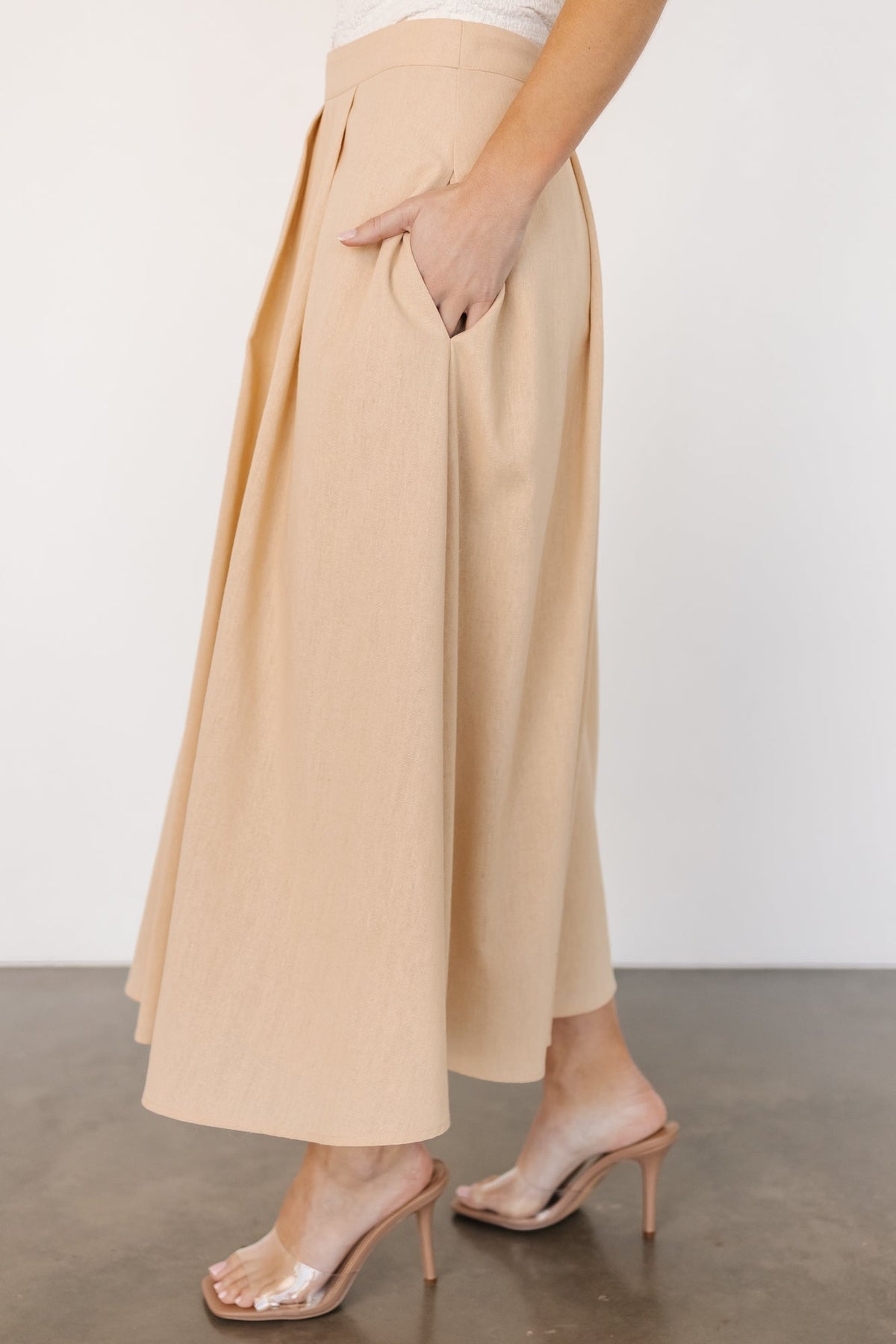 Side view of natural pleated midi skirt demonstrating hidden pocket placement, smooth lining and graceful silhouette.