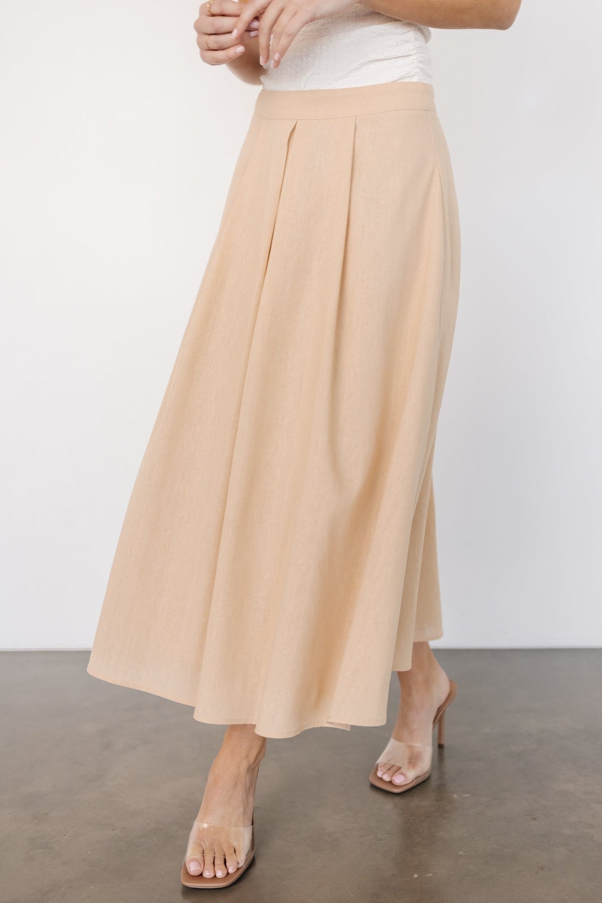 Back view of pleated midi skirt in natural color showing concealed back zipper, waistband construction and even pleat fall.