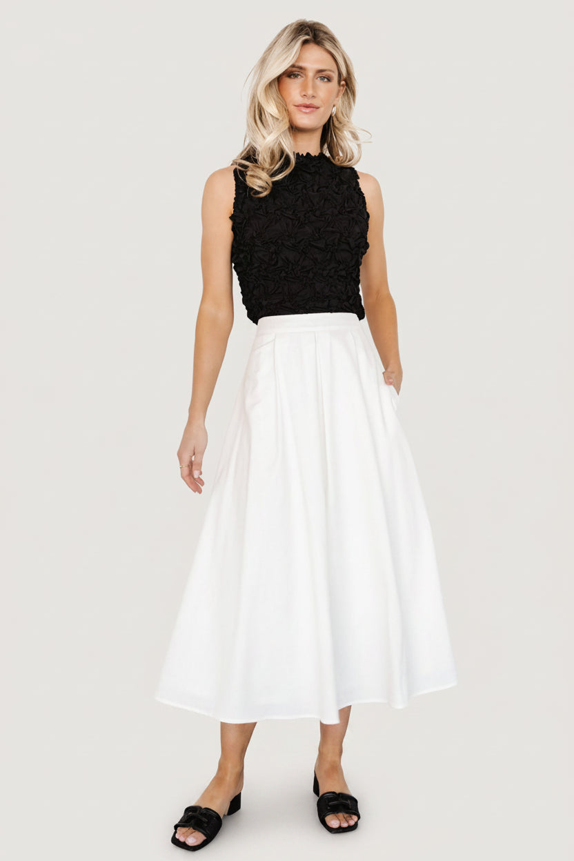 Full-length image of off-white pleated midi skirt on model with slight movement; displays skirt length, silhouette, and pocket placement.