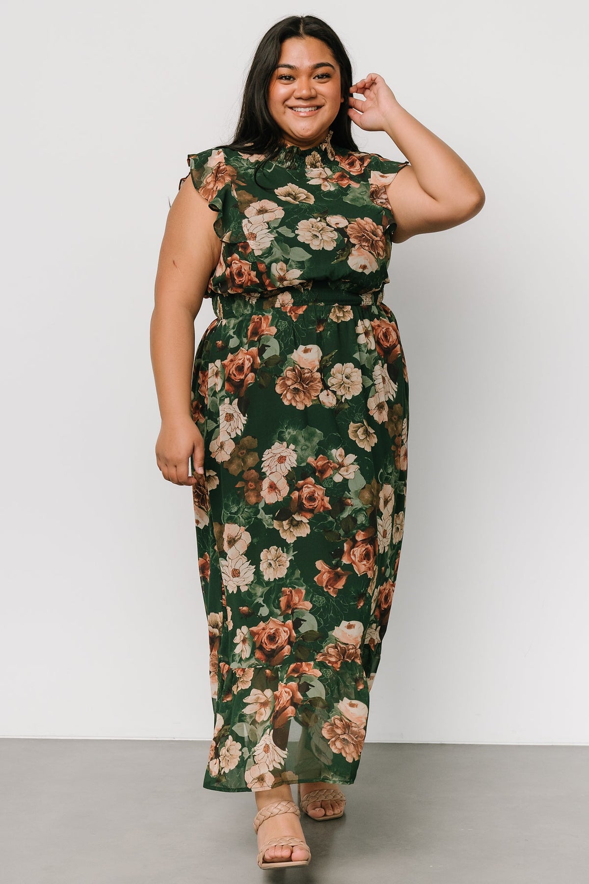 Front view of dark green floral maxi dress with smocked waist and ruffle details; delicate orange and beige floral print across fabric.