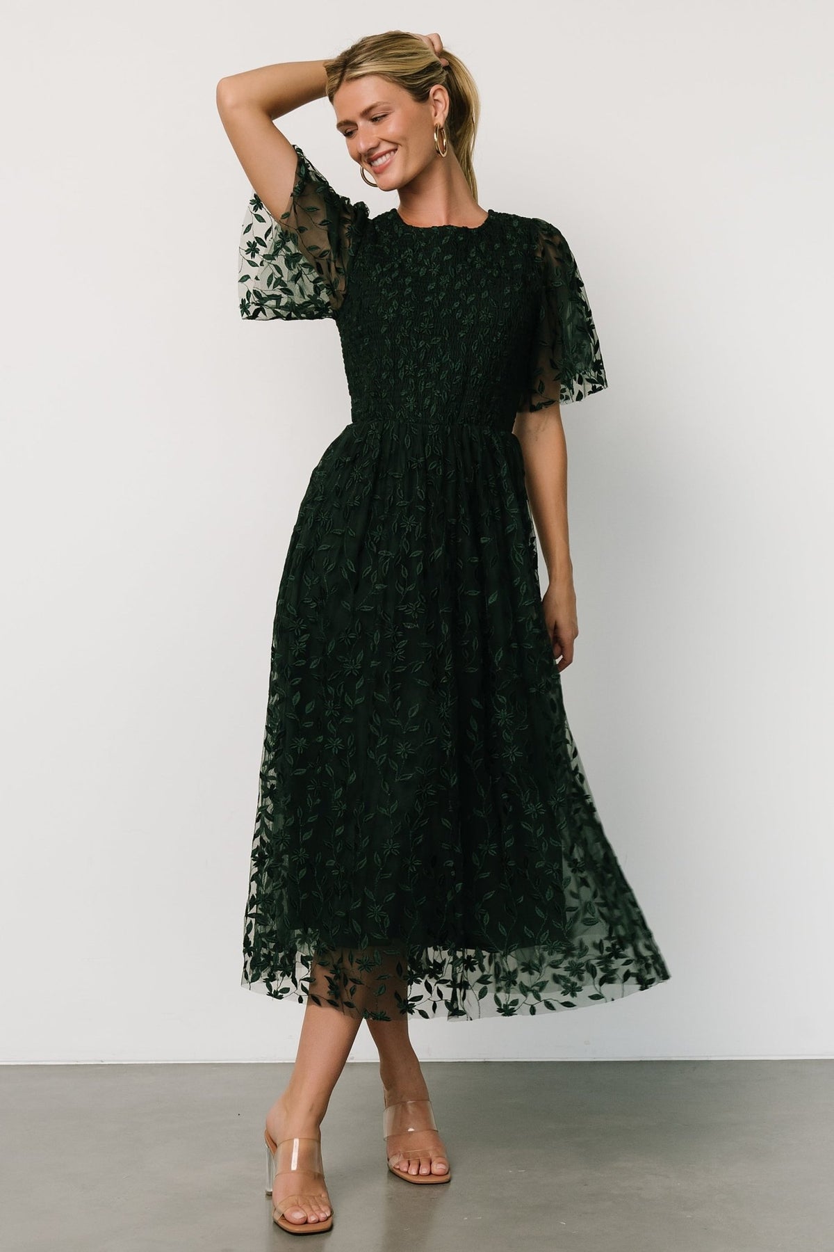 Front view of Kendra embroidered midi dress in deep green showing double-layer floral tulle, smocked bodice, and flowing midi hem.