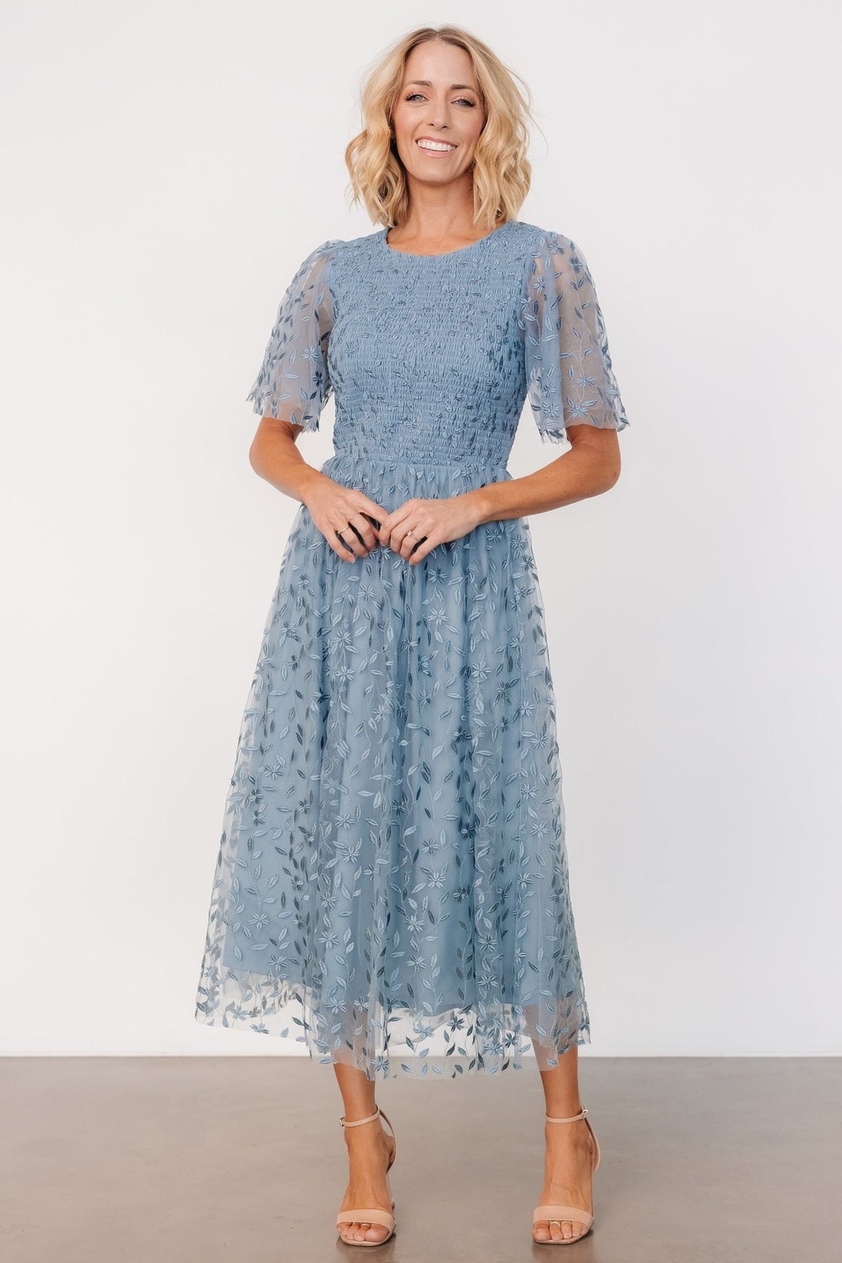 Full-length view of dusty blue embroidered midi dress with double-layer floral tulle, smocked bodice and gentle skirt drape for soft movement.