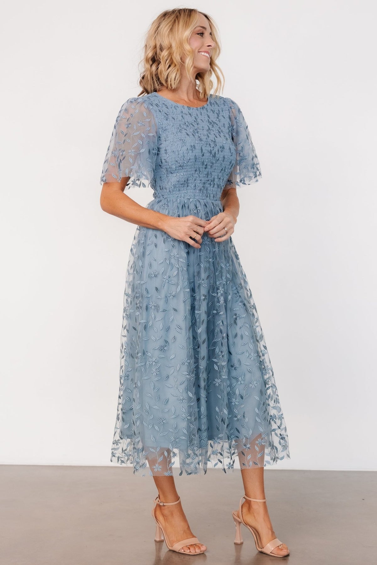 Close-up of floral embroidered tulle on dusty blue dress highlighting double-layer texture and delicate stitch detail across the skirt and bodice.