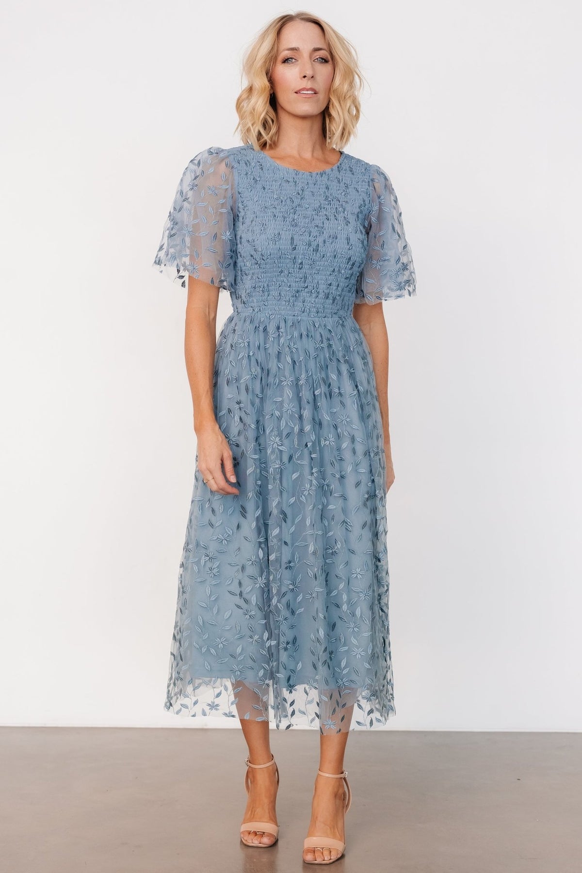 Back view showing single-button keyhole closure at the nape and the smocked bodice on the dusty blue embroidered midi dress.