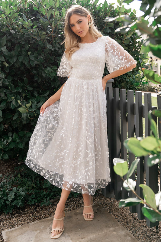 Front view of Kendra embroidered white midi dress in double-layer floral tulle with smocked bodice and flutter sleeves.