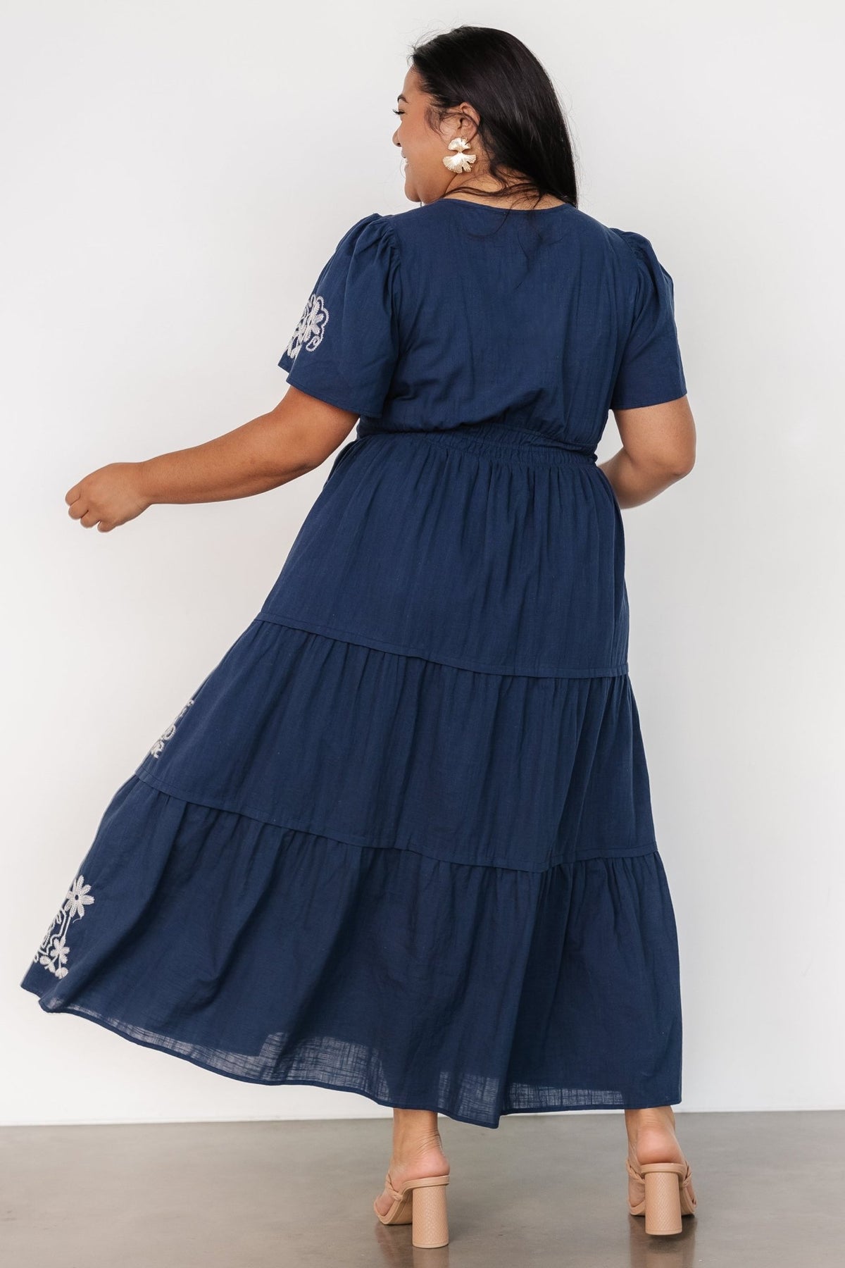 Model wearing dress walking to highlight skirt movement, tiered layers, and overall length of the maxi silhouette in blue fabric.