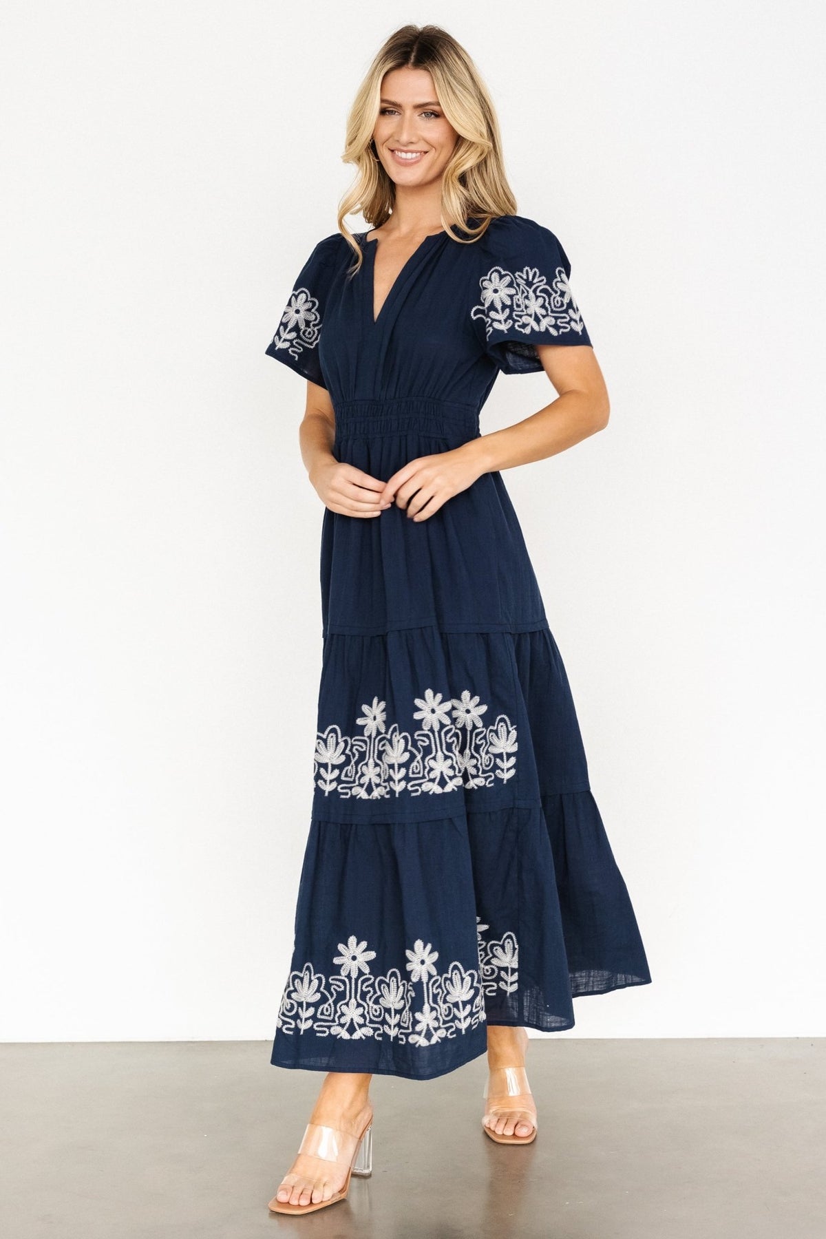 Close crop showing embroidered floral pattern on short sleeve and upper skirt with visible stitch texture on blue background.