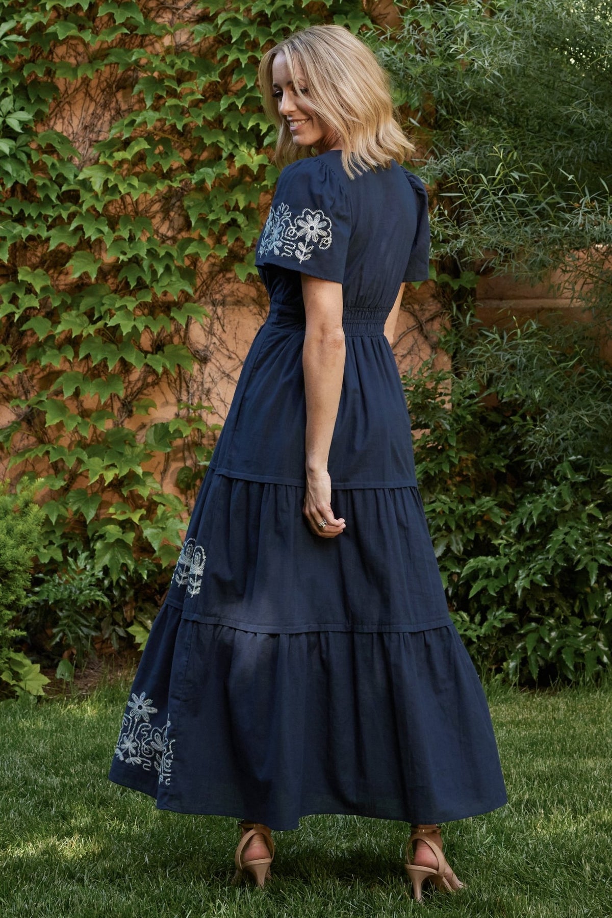 Close-up of white floral embroidery on blue skirt fabric highlighting stitch detail and embroidered floral motifs along hem.