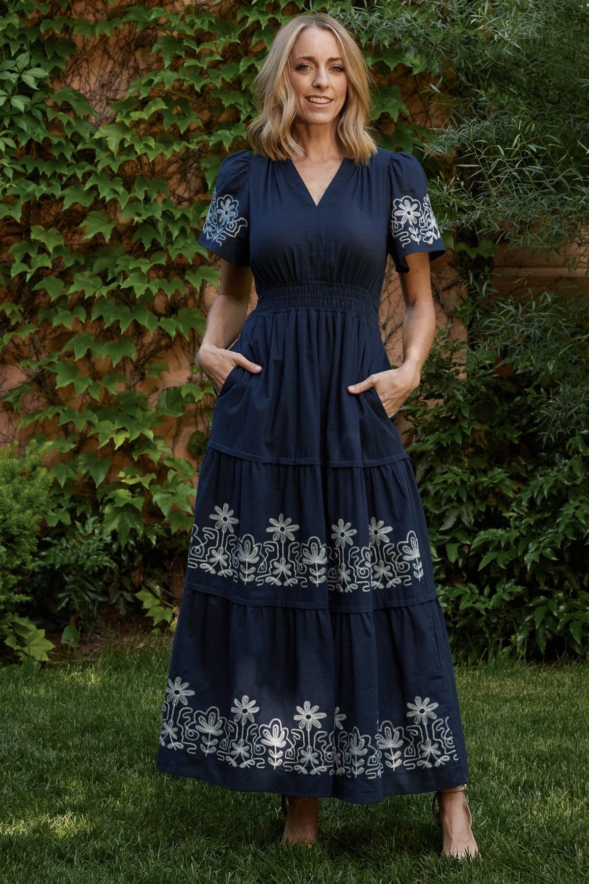 Product flat-lay of blue embroidered maxi dress showing tiered skirt layout, short sleeves, and smocked waist detail for online display.