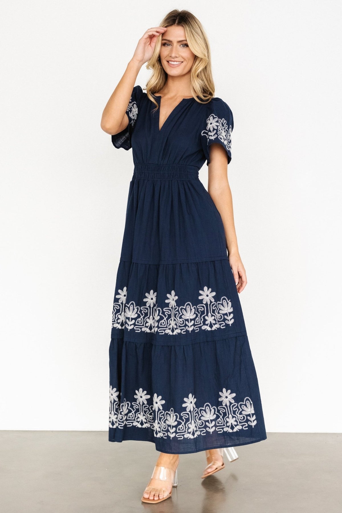 Three-quarter view showing bodice and upper skirt embroidery: notched V-neck, short sleeves, and white floral embroidery on blue fabric.