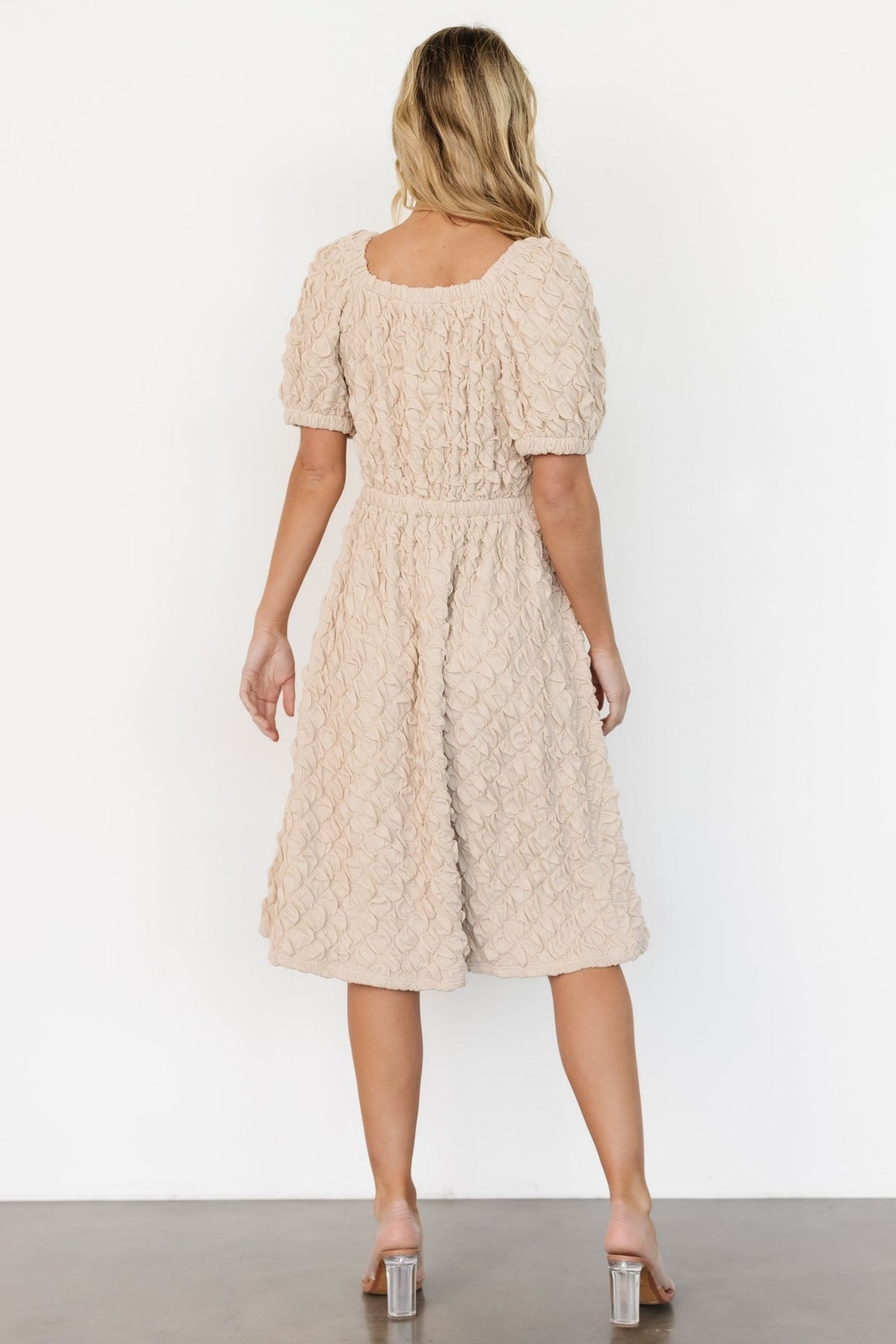 Model wearing light taupe Keri midi dress in natural light, highlighting fit through the bust and waist with the full skirt visible as she poses.