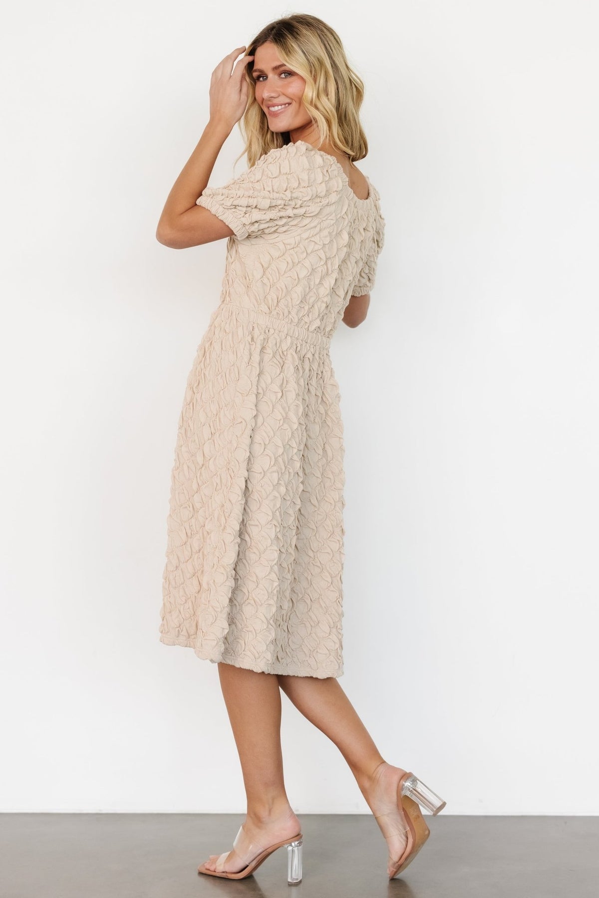 Styled flat-lay of the Keri gathered dress in light taupe, showing silhouette, sleeve shape, and neckline proportions against a neutral background.