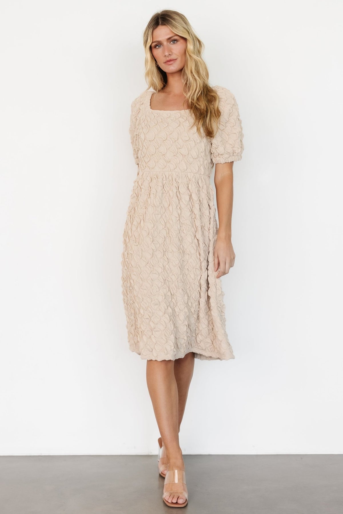 Front view of light taupe gathered midi dress on a model, showing square neckline, puff raglan sleeves, and full circle skirt movement, studio-lit.