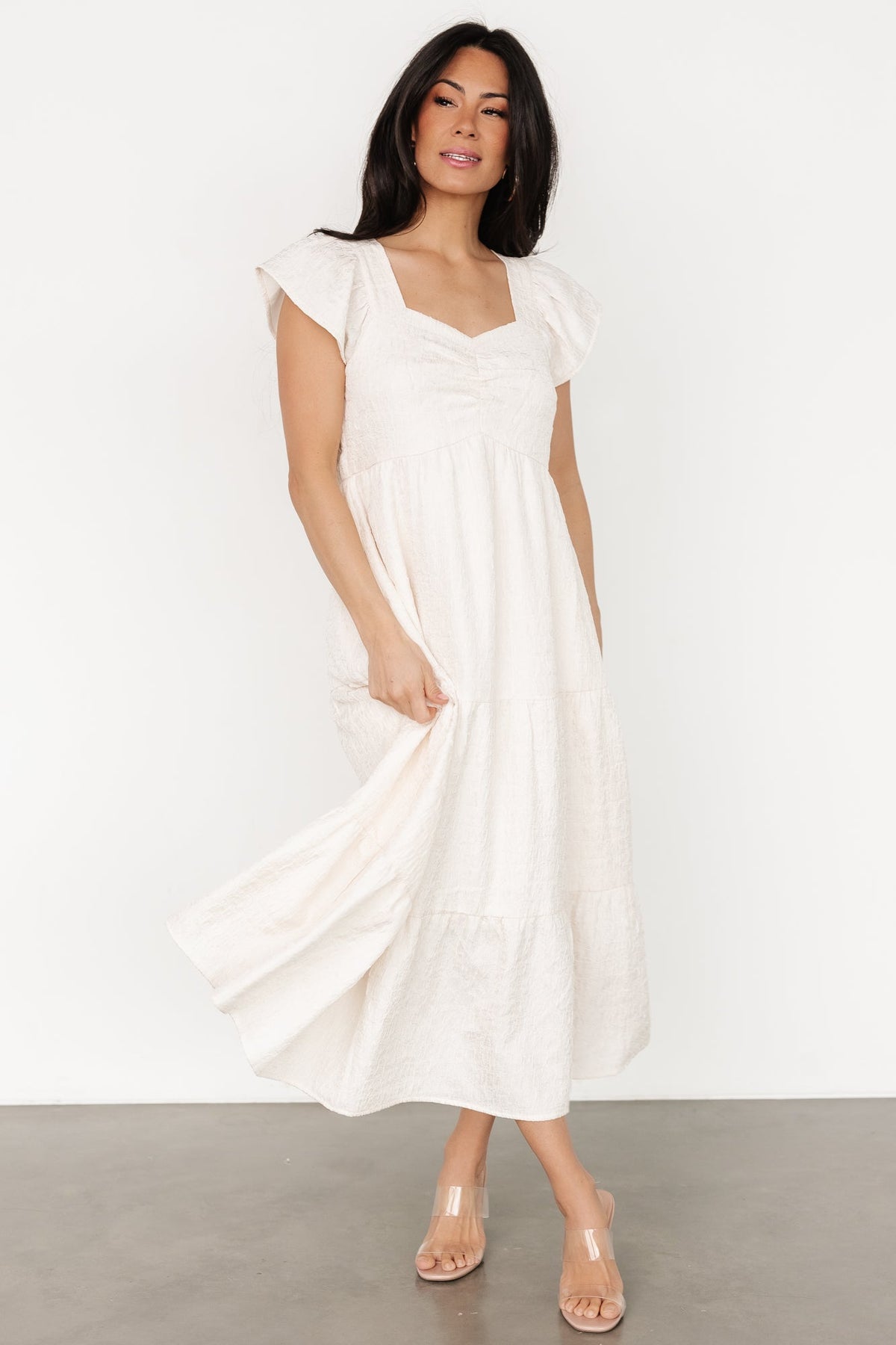 Full-length lifestyle image of Kesler Midi Dress in cream on model, displaying midi length, hidden pockets, and flowing tiers.