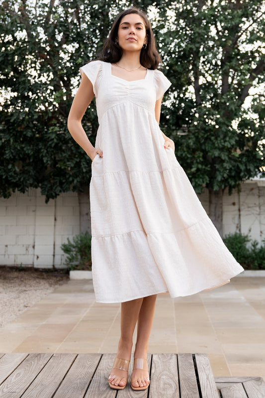 Front view of cream Kesler Midi Dress showing sweetheart neckline, smocked back bodice, cap flutter sleeves, and three-tier skirt.