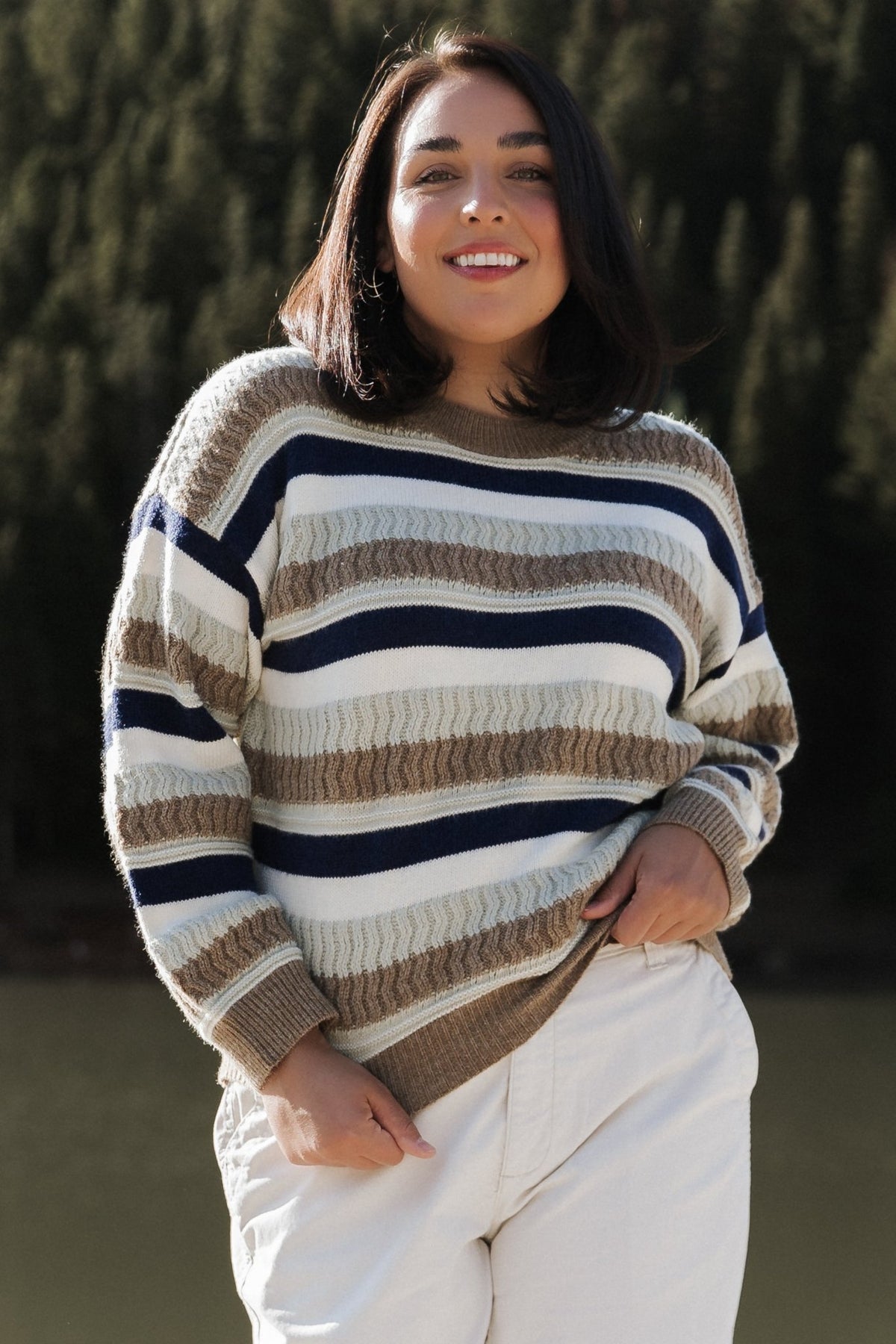 Model wearing Kira Striped Sweater in navy and sage multi-stripe, showing long sleeves, relaxed silhouette, and ribbed cuff detail.
