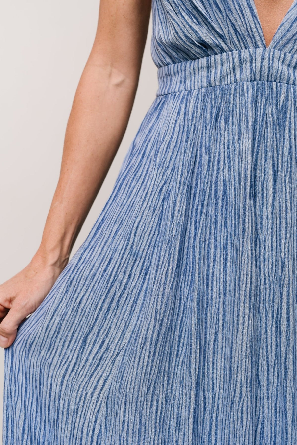 Korley Maxi Dress blue stripe styled with sandals, emphasizing the lined skirt, structured drape and event-ready silhouette.