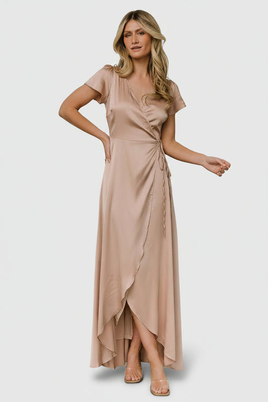 Front view of a model wearing the Krystal satin wrap gown in champagne, V-neckline, adjustable tie waist, floor-length tulip skirt and graceful drape.