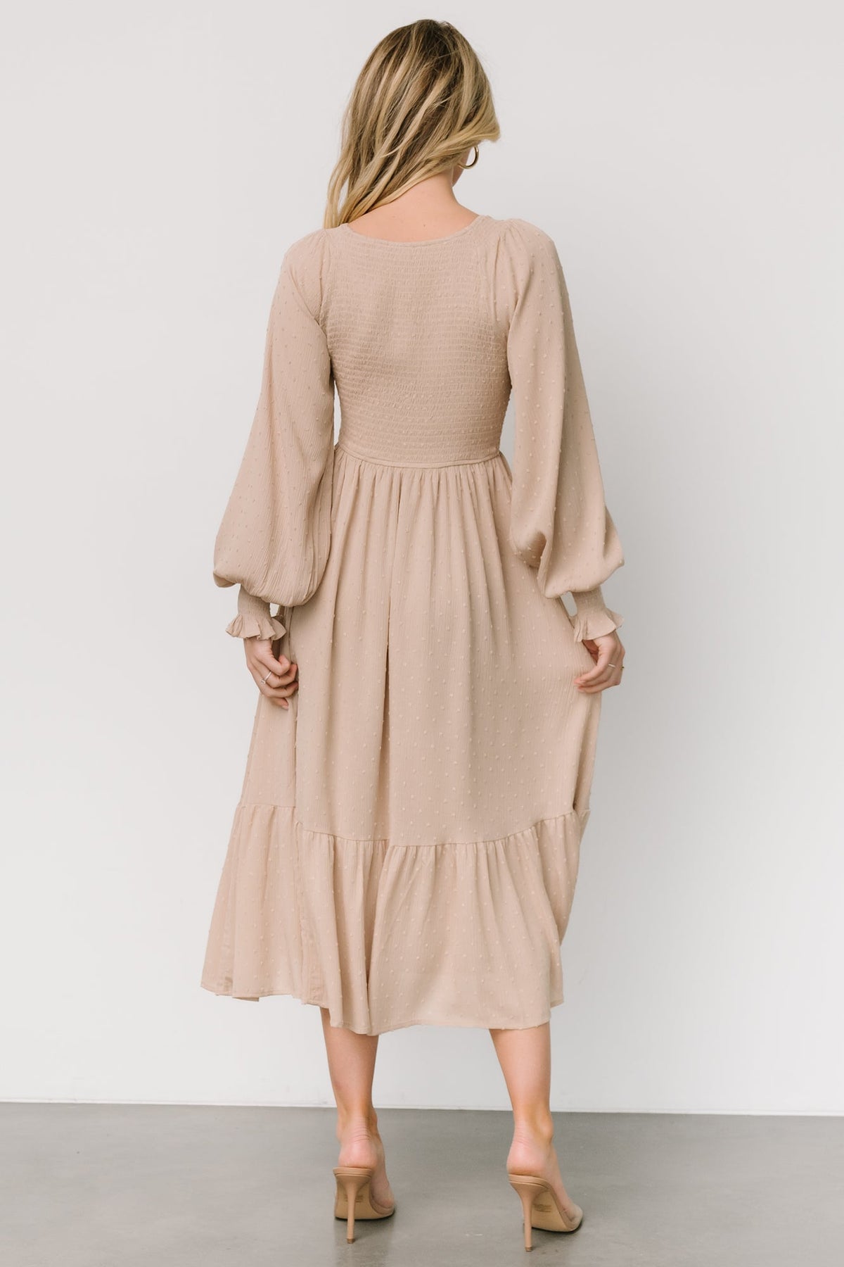 Detail shot of smocked sleeve cuff and elastic shoulder on a beige dotted midi dress, showing stitching and finish.