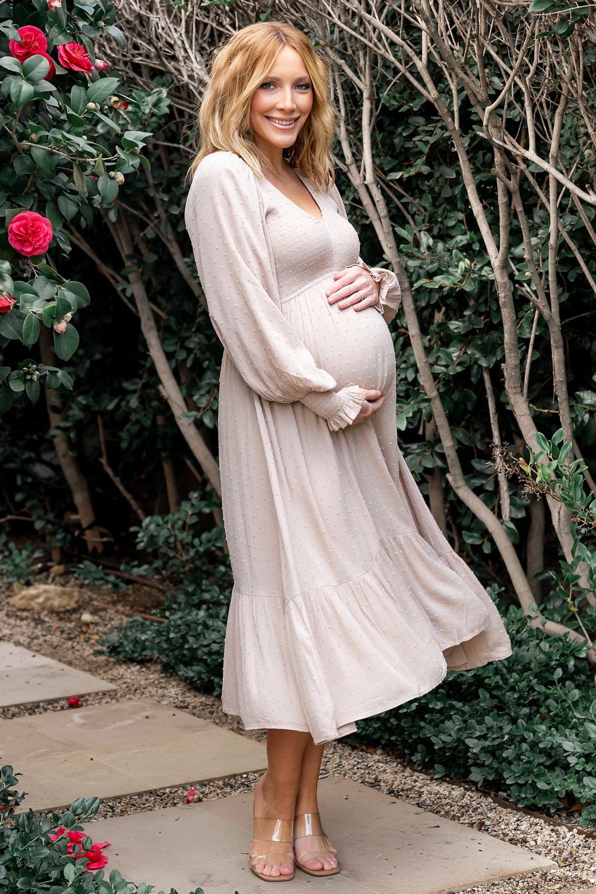 Beige dotted midi dress on model, smocked bodice, V-neck, long sleeves and tiered hem, front view with natural drape (model wearing dress).