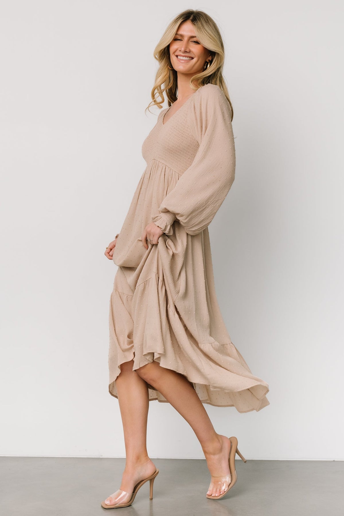 Full-length view of beige dotted midi dress on model, tiered hem and gentle drape from high V-waist to mid-calf.