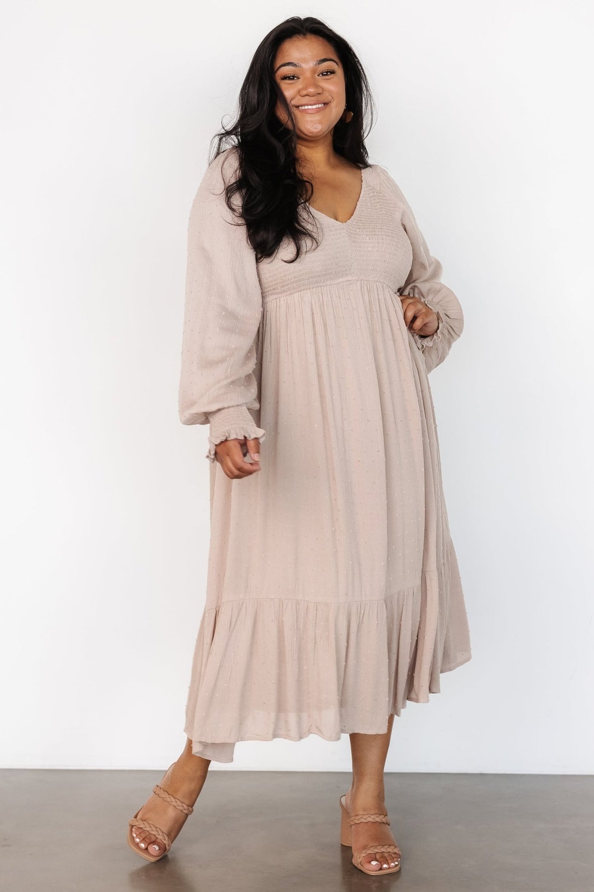 Side view of beige dotted midi dress on model showing smocked cuffs, elastic shoulders, and the tiered skirt silhouette.