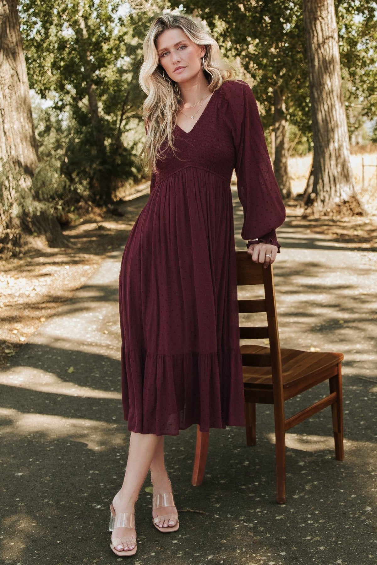 Front view of Lainey smocked dotted midi dress in rich mulberry, showing V-neck, smocked bodice, long sleeves, and tiered hem for styling.