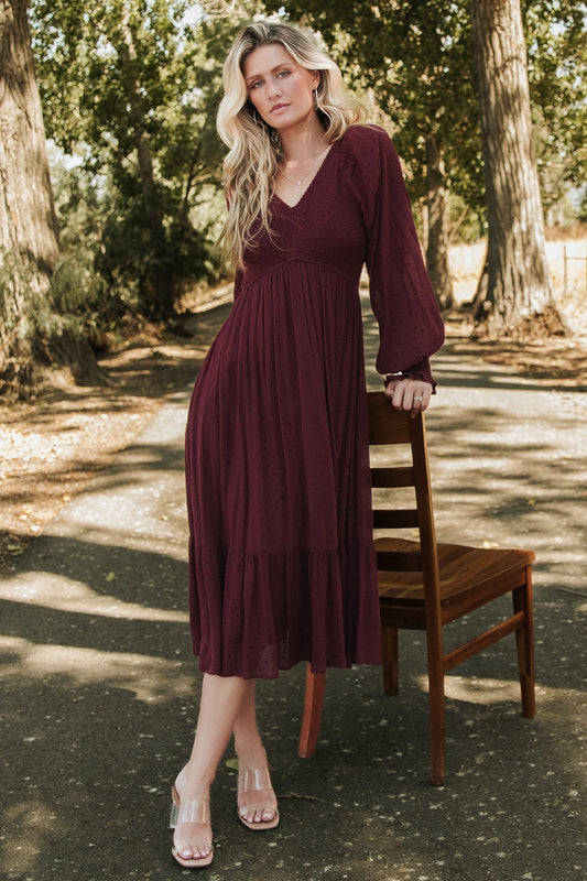 Front view of Lainey smocked dotted midi dress in rich mulberry, showing V-neck, smocked bodice, long sleeves, and tiered hem for styling.