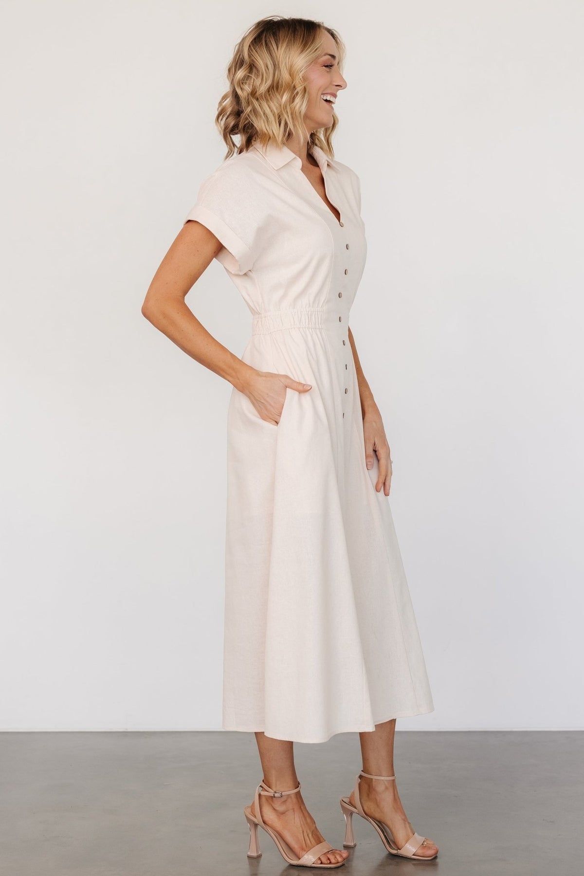 Back view highlighting the fully smocked back waistband on the natural linen-cotton midi dress, showing fit and gathered detail at the waist.
