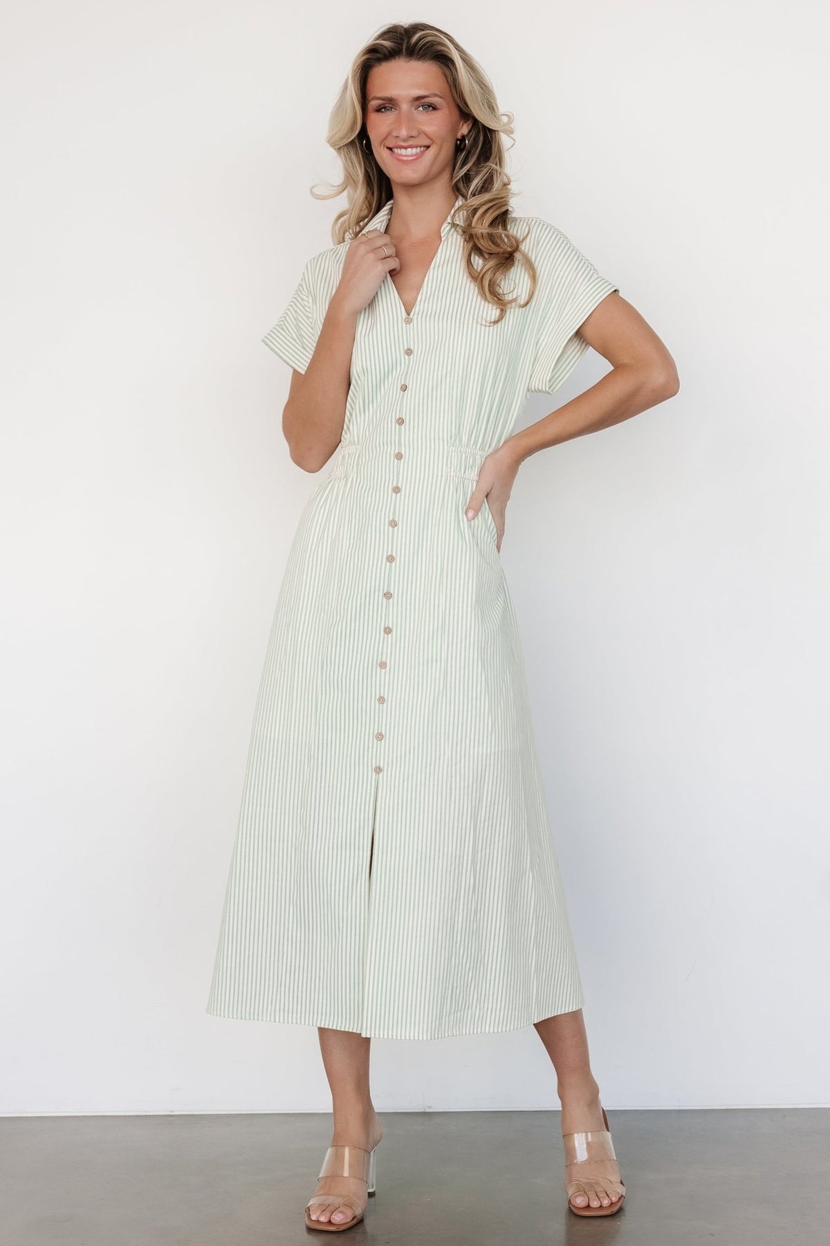 Three-quarter view of midi dress in sage stripe showing vertical front seams, faux buttons, and partially smocked front waistband.