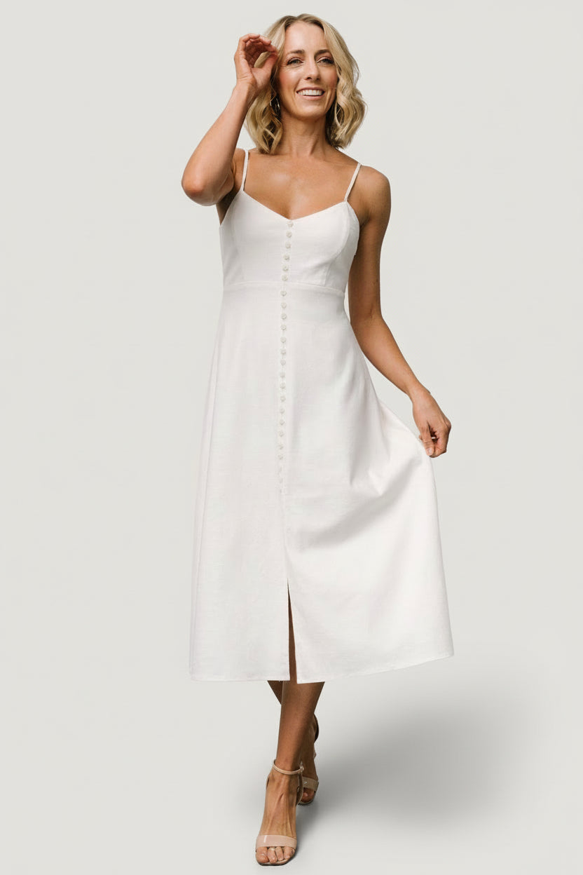 Full-length shot of an ivory cotton-linen midi dress on model showing button-front design, adjustable straps, and flowing hem for versatile styling.