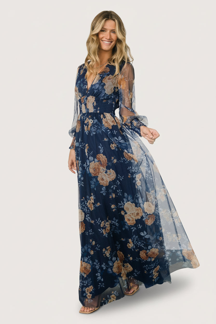 Model wearing Layla blue golden floral maxi dress in studio, full-length pose showing floor-grazing silhouette and deep V-neck styling.