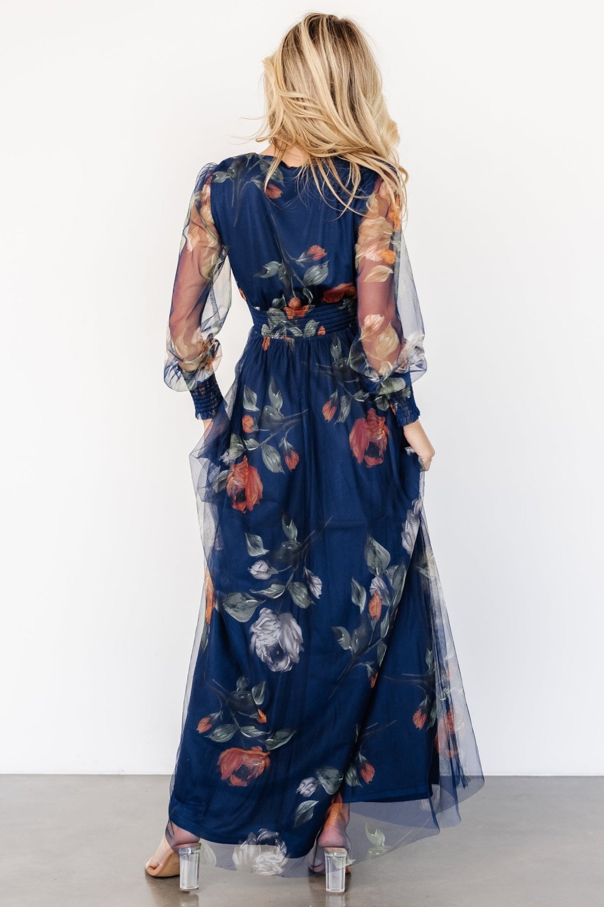 Detail view of long sheer sleeve with smocked cuff and delicate floral tulle overlay on navy background.
