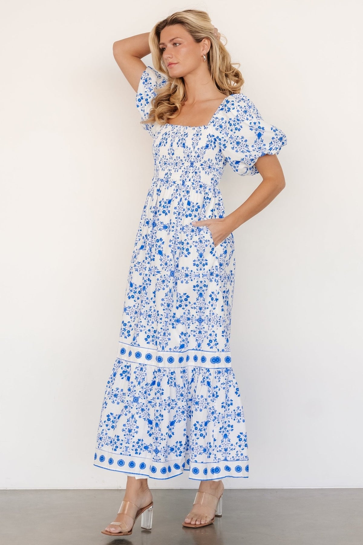 Back view showing tiered maxi skirt and gentle flare, off-white fabric with blue floral print and elastic at the waist for shape.